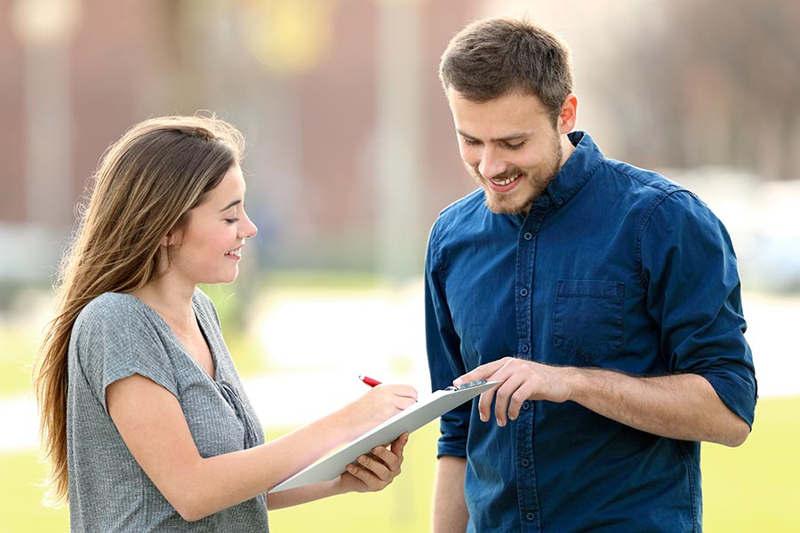 Das Bild zeigt eine Frau und einen Mann im Gespräch, wobei die Frau etwas auf einem Blatt Papier notiert.