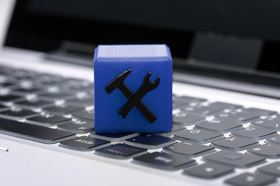 The picture shows a cube with a black hammer and a black hexagon wrench lying on a notebook keyboard.