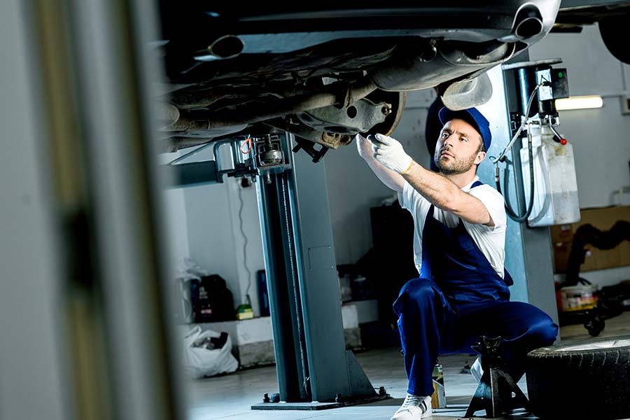 Das Bild zeigt einen Automechaniker, der in einer Werkstatt ein Fahrzeug repariert.