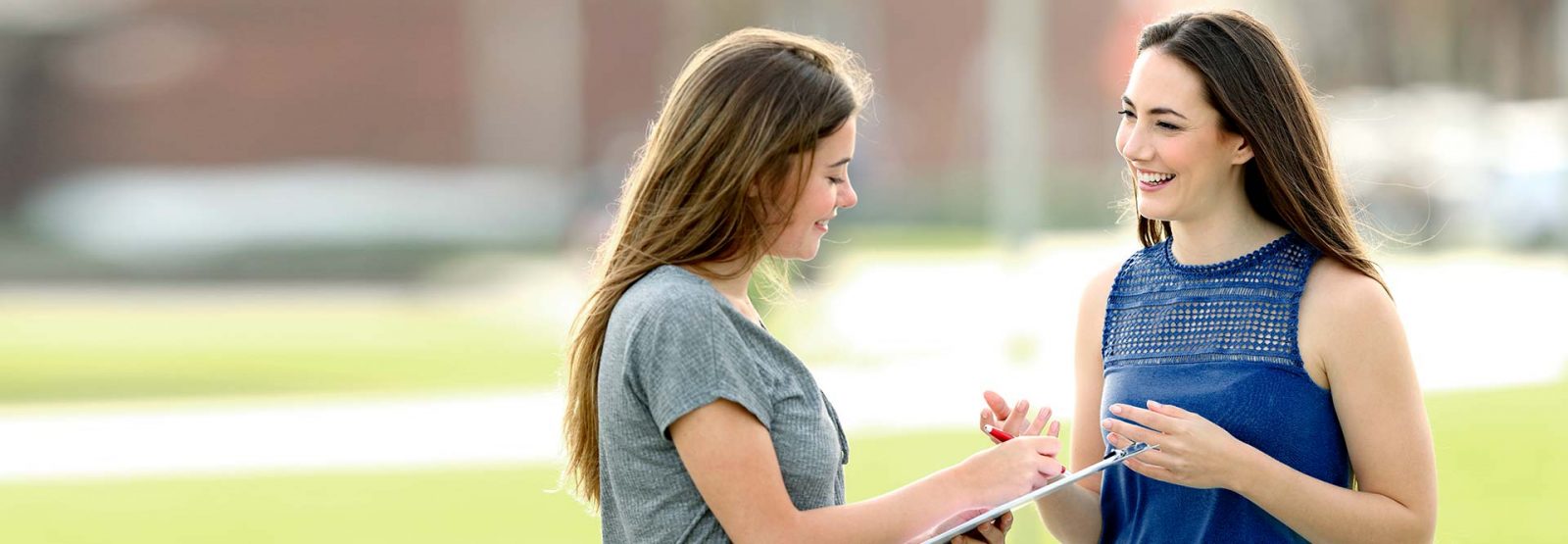 The picture shows two women having a conversation while one of them is taking some notes on a sheet of paper.