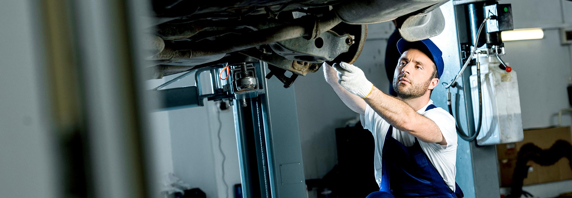 The picture shows a car mechanic repairing a vehicle at the garage.