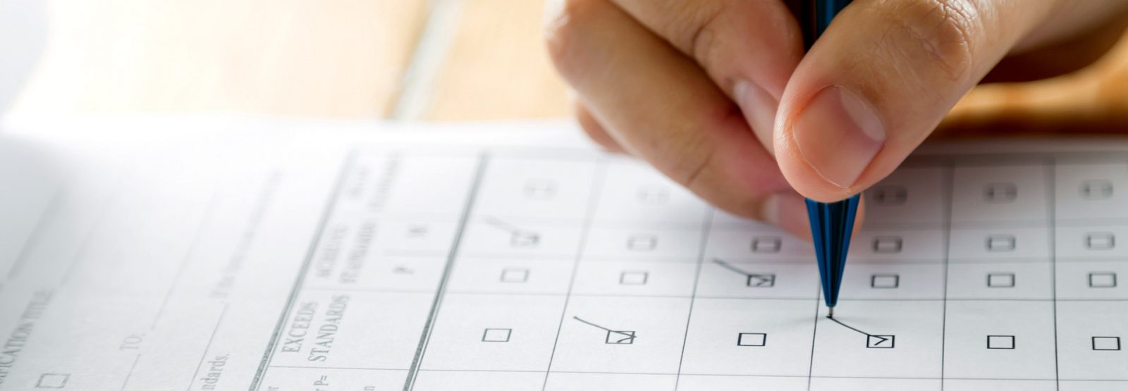 The picture shows a hand filling in a questionnaire with a pen.