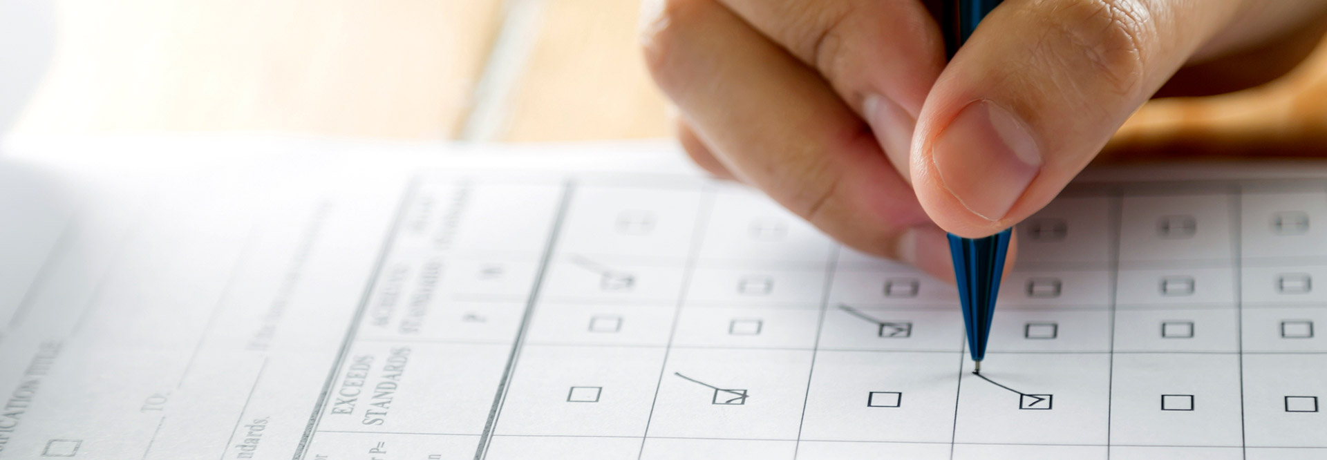 The picture shows a hand filling in a questionnaire with a pen.