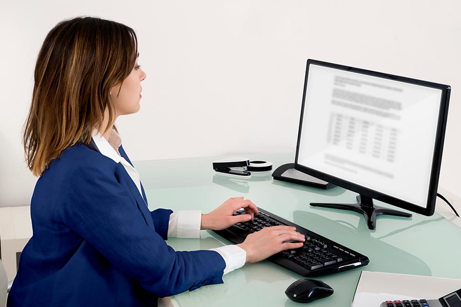Das Bild zeigt eine Frau im Blazer am Schreibtisch vor dem Computer.