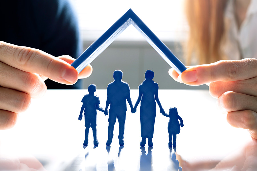 Two hands are holding a roof above the silhouette of a family.