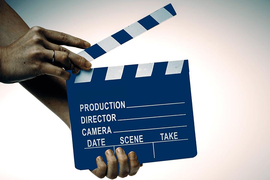 The picture shows a clapperboard held by two hands.