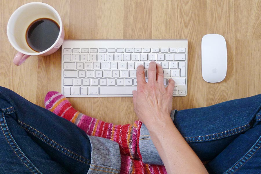 Das Bild zeigt eine auf dem Boden sitzende Person. Vor der Person auf dem Boden liegt eine Tastatur, eine Computermaus und eine Tasse Kaffee.